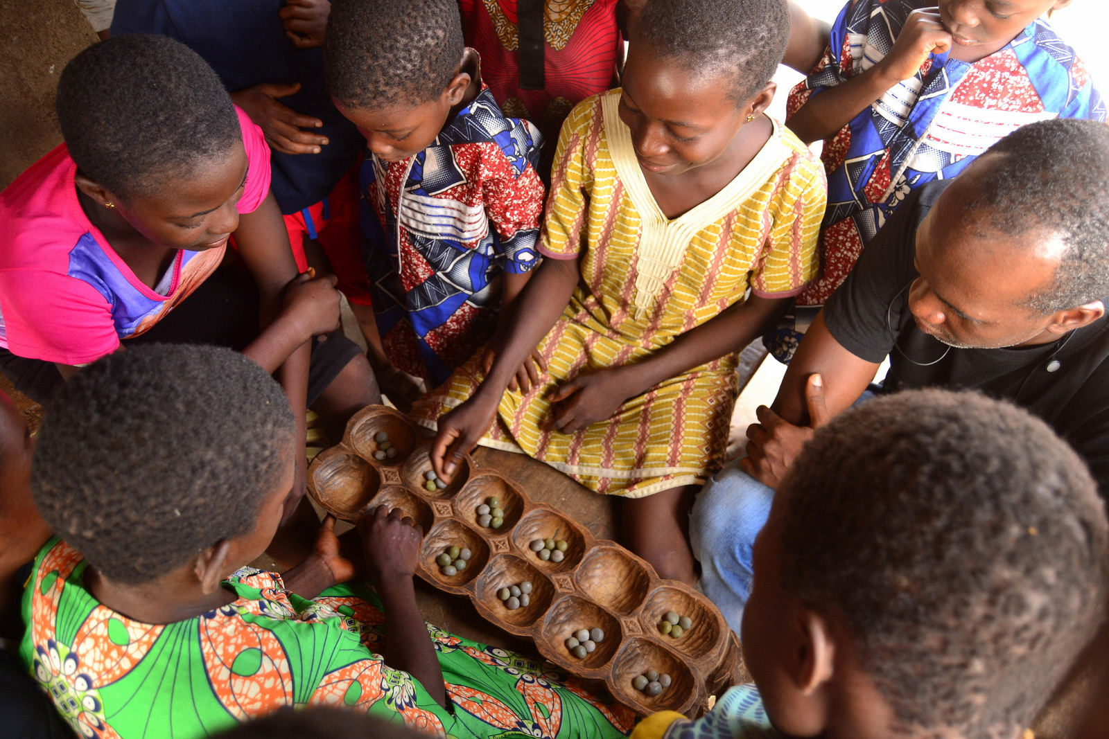 Children gather around a game of Ayo